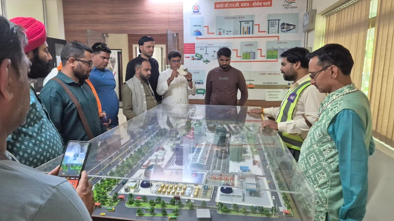 इंदौर संयंत्र में प्रतिनिधिमंडल एक मेज पर रखा गोबर-धन प्लांट का मॉडल देख रहा है